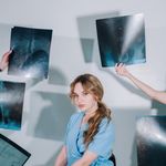 A female healthcare worker in blue scrubs reviews multiple X-ray images indoors.